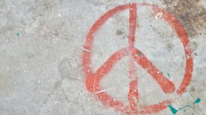 Betongbakgrund med den internationella fredssymbolen målad i röd grafitti.